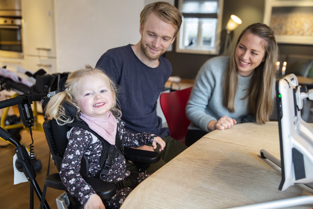 Ella har lyse musefletter og smiler til kamera. Hun har tobiien foran seg på bordet. Til høyre for henne sitter pappa Kim og mamma Malin, begge ser på Ella og smiler.