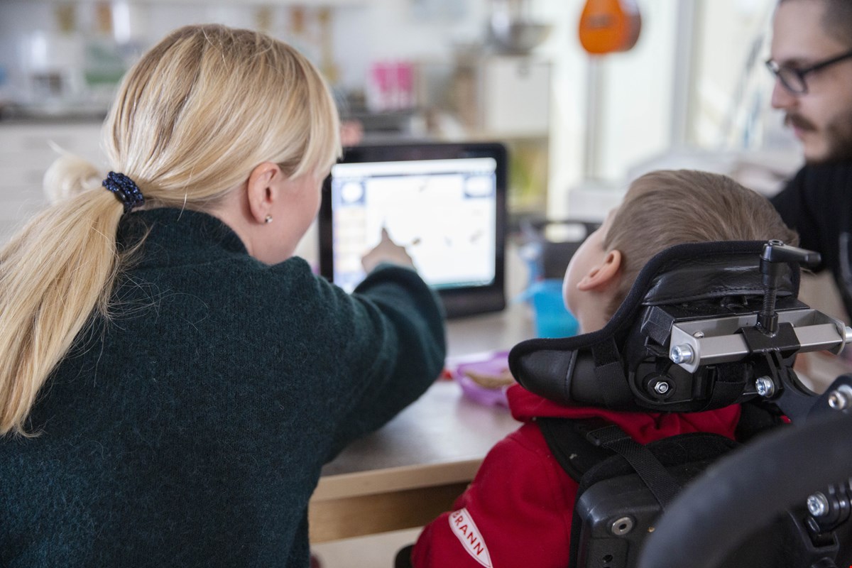 Bildet viser bakhodet til Torbjørn og assistenten Linda.  Linda har langt lyst hår i hestehale og Torbjørn har kort brunt hår. Linda peker på Tobii-skjermen som er uklar foran dem.